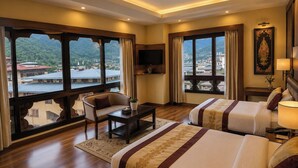 Una habitación de hotel con una cama grande, una cama más pequeña, un escritorio, una silla, un televisor y vistas a un paisaje montañoso.