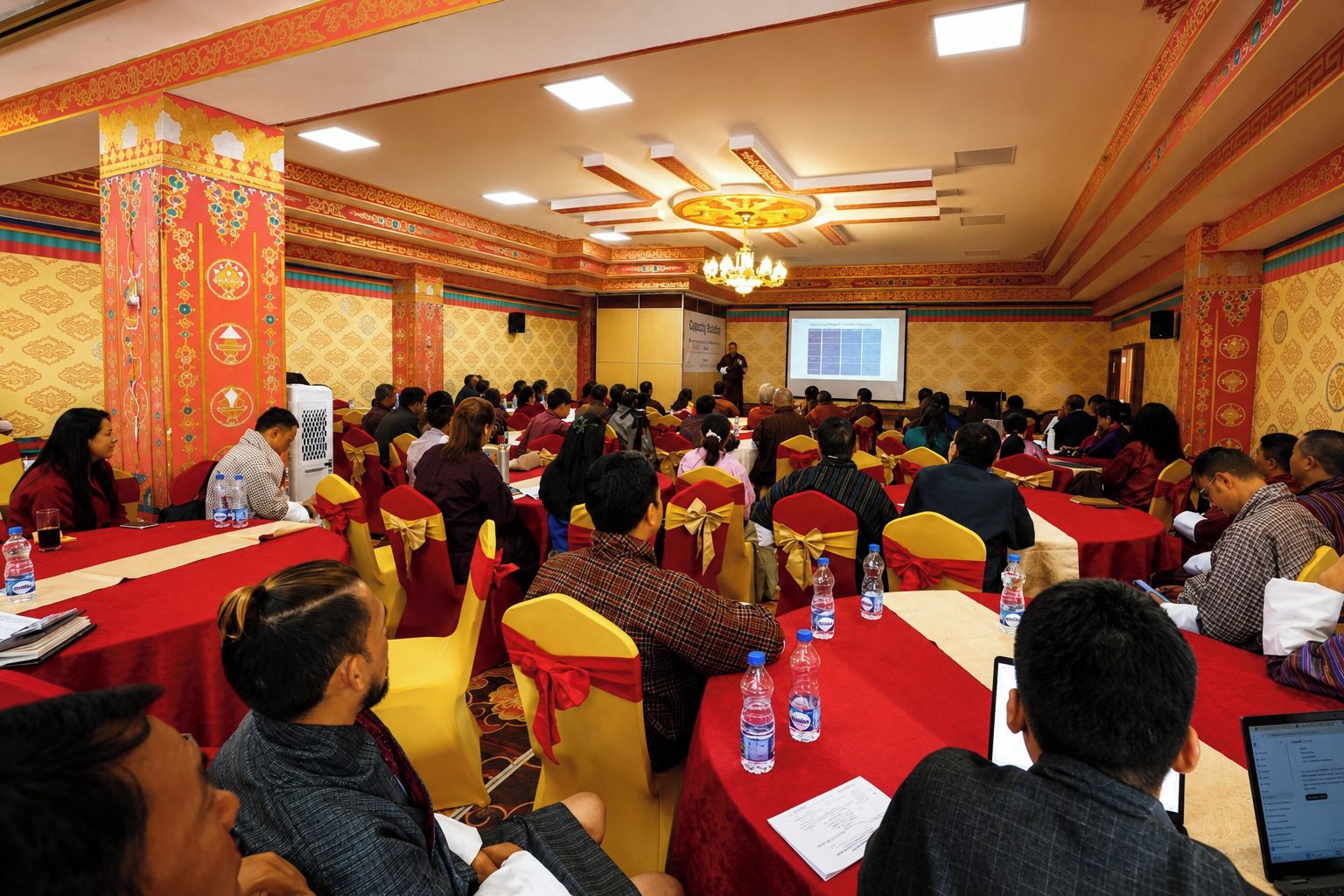 A conference room with round tables, attendees seated, and a presentation screen.