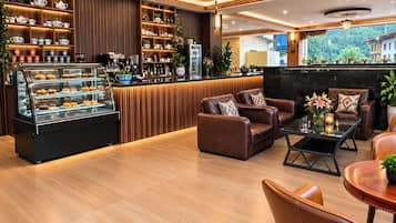 A modern lounge area with leather sofas, a coffee station, and a display case of pastries.
