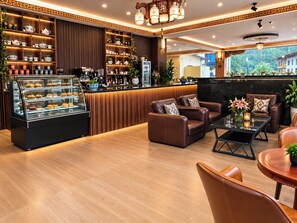 A modern lounge area with leather sofas, a coffee station, and a display case of pastries.