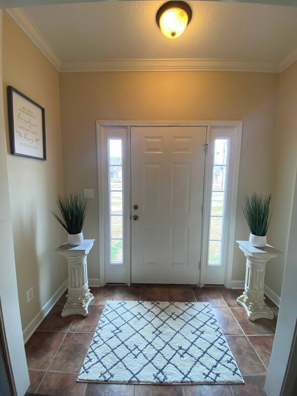 A hallway with a white door, two potted plants on pedestals, a patterned rug, and a ceiling light. - Classic connection in the Hub City! (Jackson)