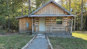 Una baita di legno con un portico, un vialetto sterrato e uno sfondo boschivo.