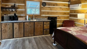Una compatta cabina di legno con angolo cottura, un letto e un piccolo spazio per sedersi.