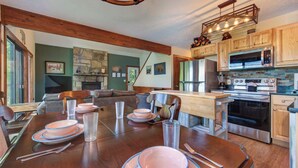 Une cuisine spacieuse avec des meubles en bois, un coin repas doté d’une grande table pouvant accueillir quatre personnes, et une cheminée en pierre.