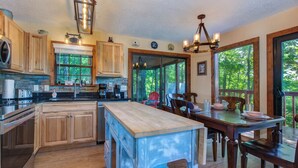 Une cuisine spacieuse, dotée de meubles en bois, d’un îlot central et de grandes fenêtres offrant une vue sur l’extérieur.