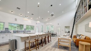 A spacious kitchen with a large island, bar stools, and a dining area with a sofa and coffee table. - 3-Acre Luxury 5BR Ranch, Movie Theater, 2 Kitchens, Near COTA Airport! Sleeps 14 (Austin)