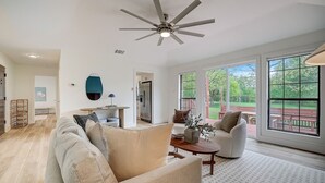 A spacious living room with a ceiling fan, a sofa, a coffee table, and a view of a patio with outdoor furniture. - 3-Acre Luxury 5BR Ranch, Movie Theater, 2 Kitchens, Near COTA Airport! Sleeps 14 (Austin)