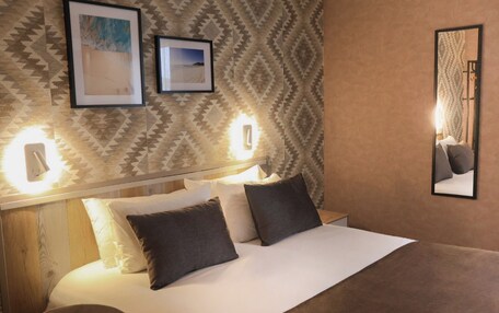 A neatly made bed with a headboard, two framed pictures on the wall, and a mirror.