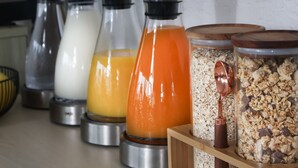 Un plan de travail de cuisine avec divers récipients contenant des aliments, notamment un mixeur, une bouteille de lait, une bouteille de jus et un récipient de granola.