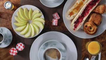 A breakfast setting with a plate of sliced apples, a cup of coffee, a glass of orange juice, and pastries.