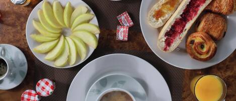 A breakfast setting with a plate of sliced apples, a cup of coffee, a glass of orange juice, and pastries.