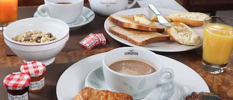 Een ontbijttafel met een kom ontbijtgranen, een croissant, een kop koffie, toast, jam en een glas sinaasappelsap.