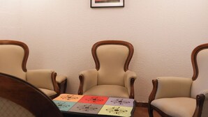 Une pièce comprenant deux fauteuils rembourrés, une petite table ornée d’un motif géométrique coloré et un tableau encadré représentant un coucher de soleil accroché au mur.