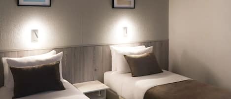 A hotel room with two single beds, each with a pillow and a bedside table.