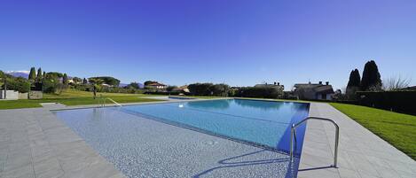 Une piscine rectangulaire à l’eau d’un bleu limpide, entourée d’une terrasse carrelée et d’une rambarde métallique.