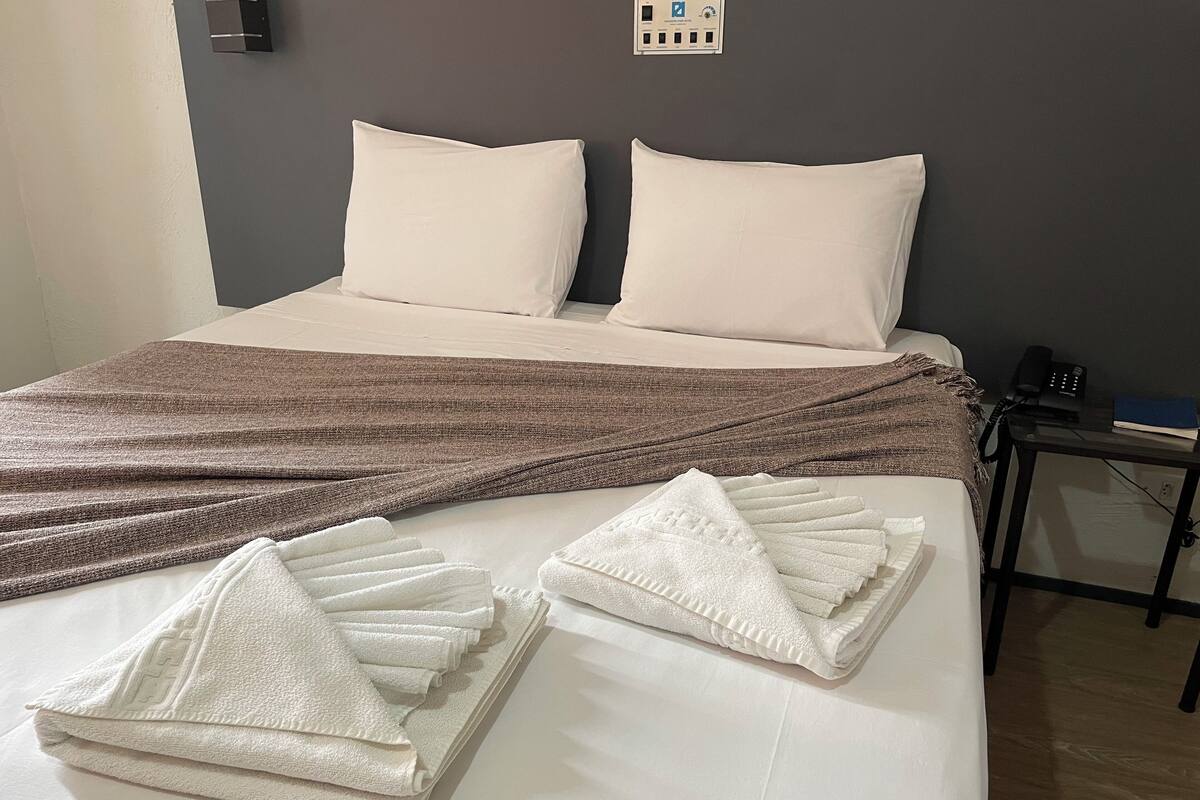 A neatly made bed with a brown blanket, two pillows, and two folded towels.