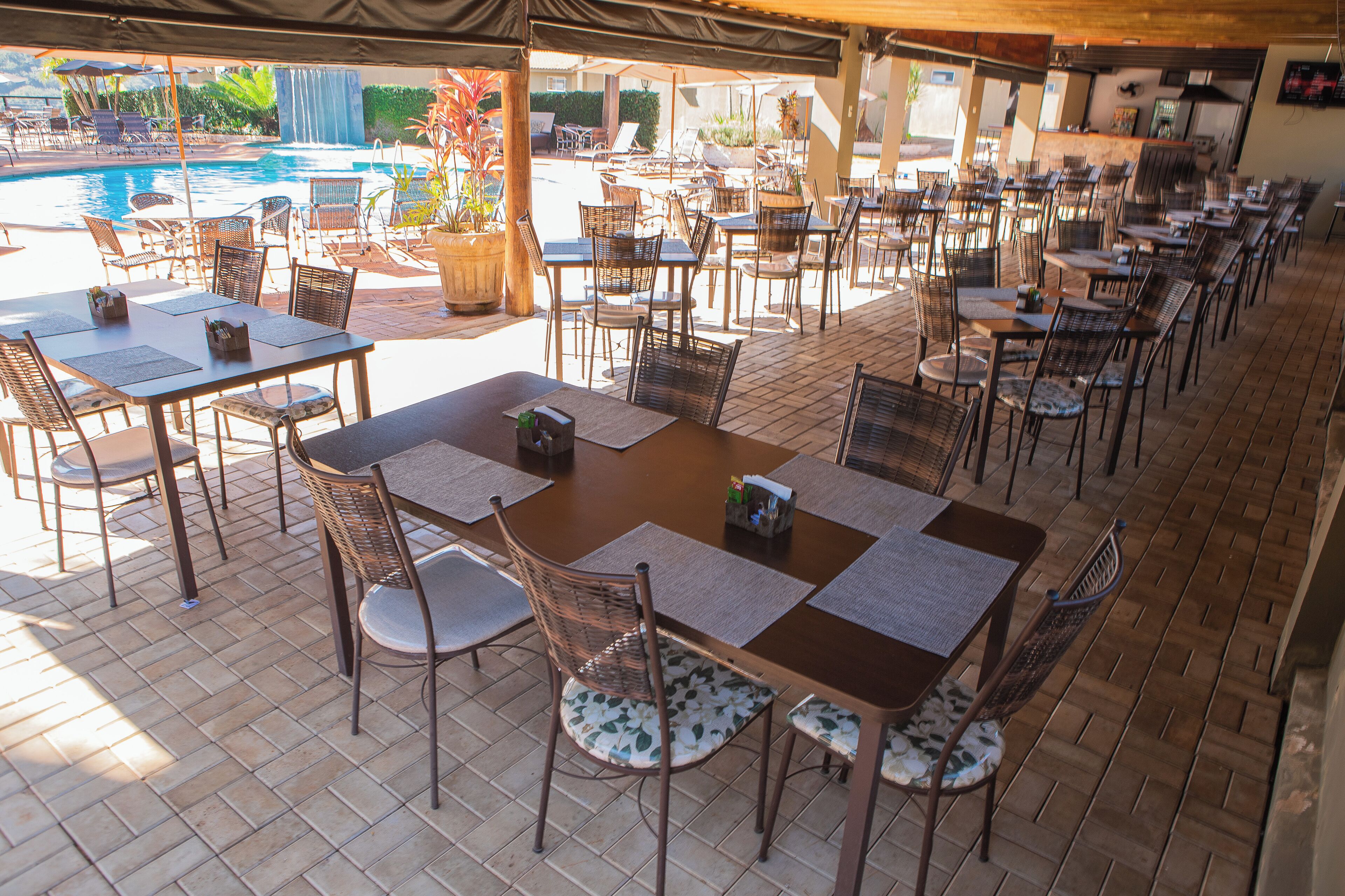 Un espace de restauration en plein air avec plusieurs tables et chaises, une piscine en arrière-plan et un coin salon abrité.