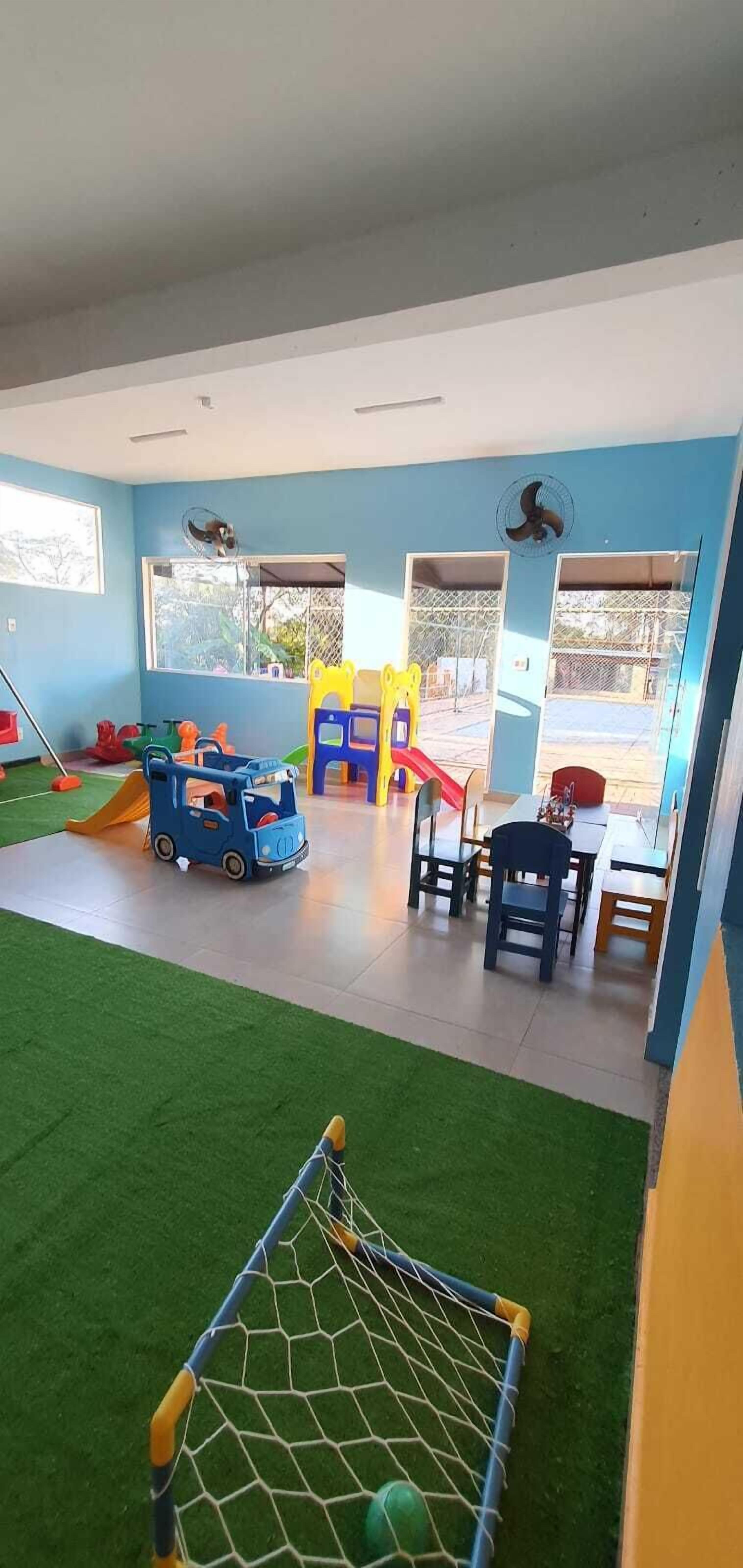 Un espace de jeux pour enfants avec un but de football, des structures de jeu et une petite voiture bleue.