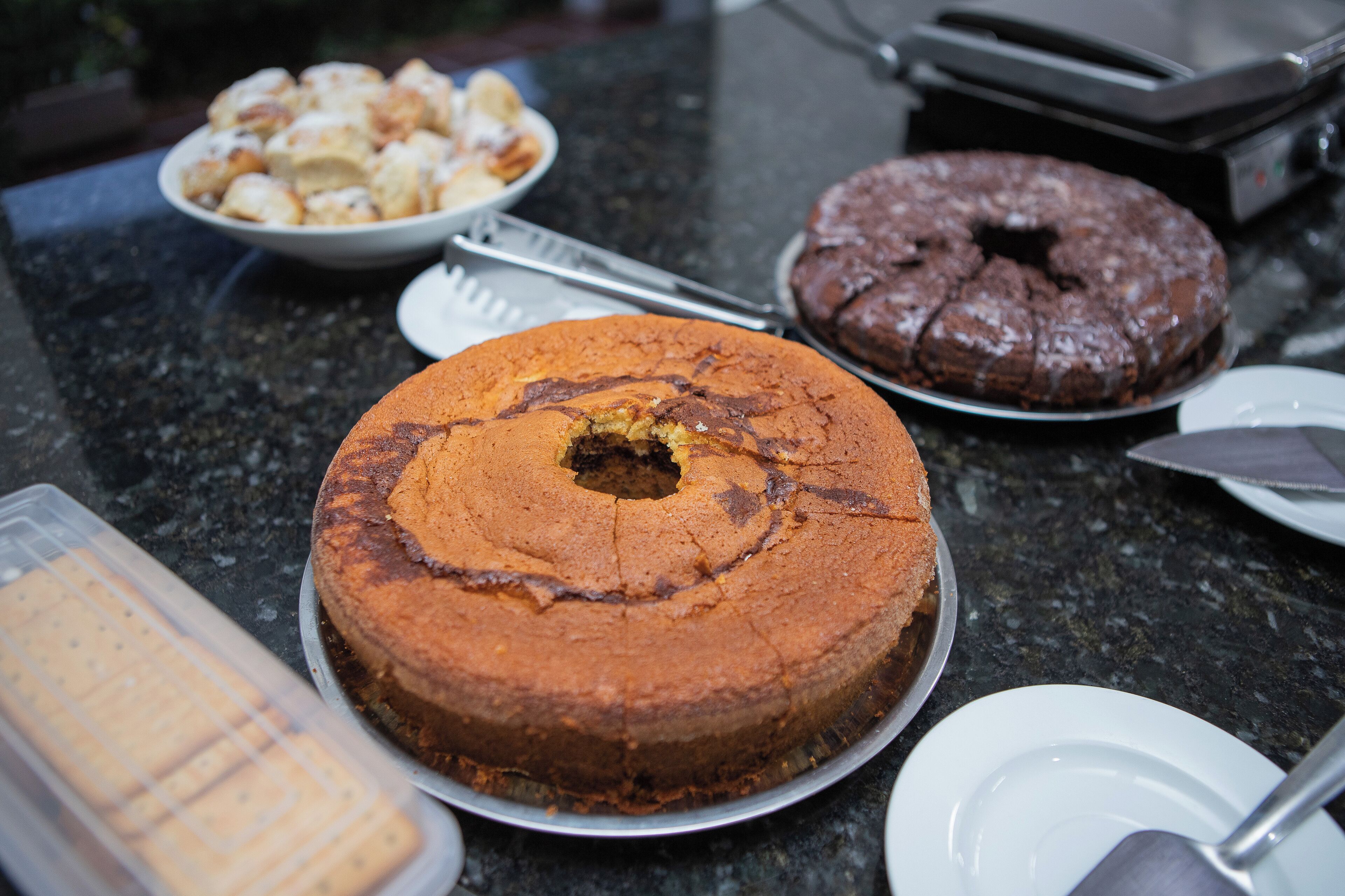 A countertop with a chocolate cake, a plate of cookies, and a cake server.