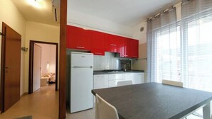 Une cuisine de taille réduite avec des meubles de couleur rouge, un réfrigérateur blanc et un coin repas comprenant une table et des chaises.