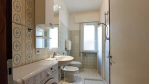 Une petite salle de bain équipée d’un lave-linge, d’un lavabo, de toilettes et d’un bidet.