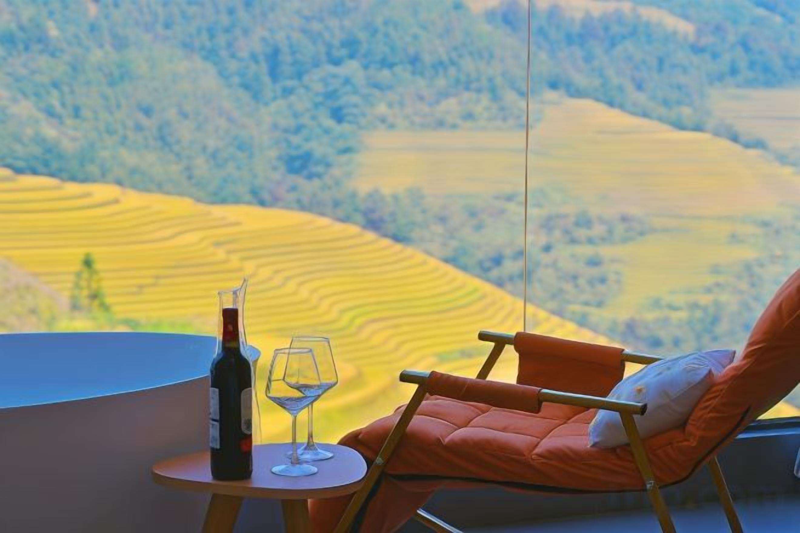 Une terrasse avec une table, une bouteille de vin et un verre, donnant sur des champs en terrasses.