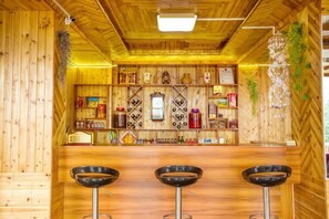 A bar area with wooden walls, a counter, and three stools. - Xiyu Boutique Hostel (Longsheng)