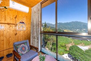 A wooden interior with a view of mountains, a chair with a patterned cushion, and a table with a plant. - Xiyu Boutique Hostel (Longsheng)