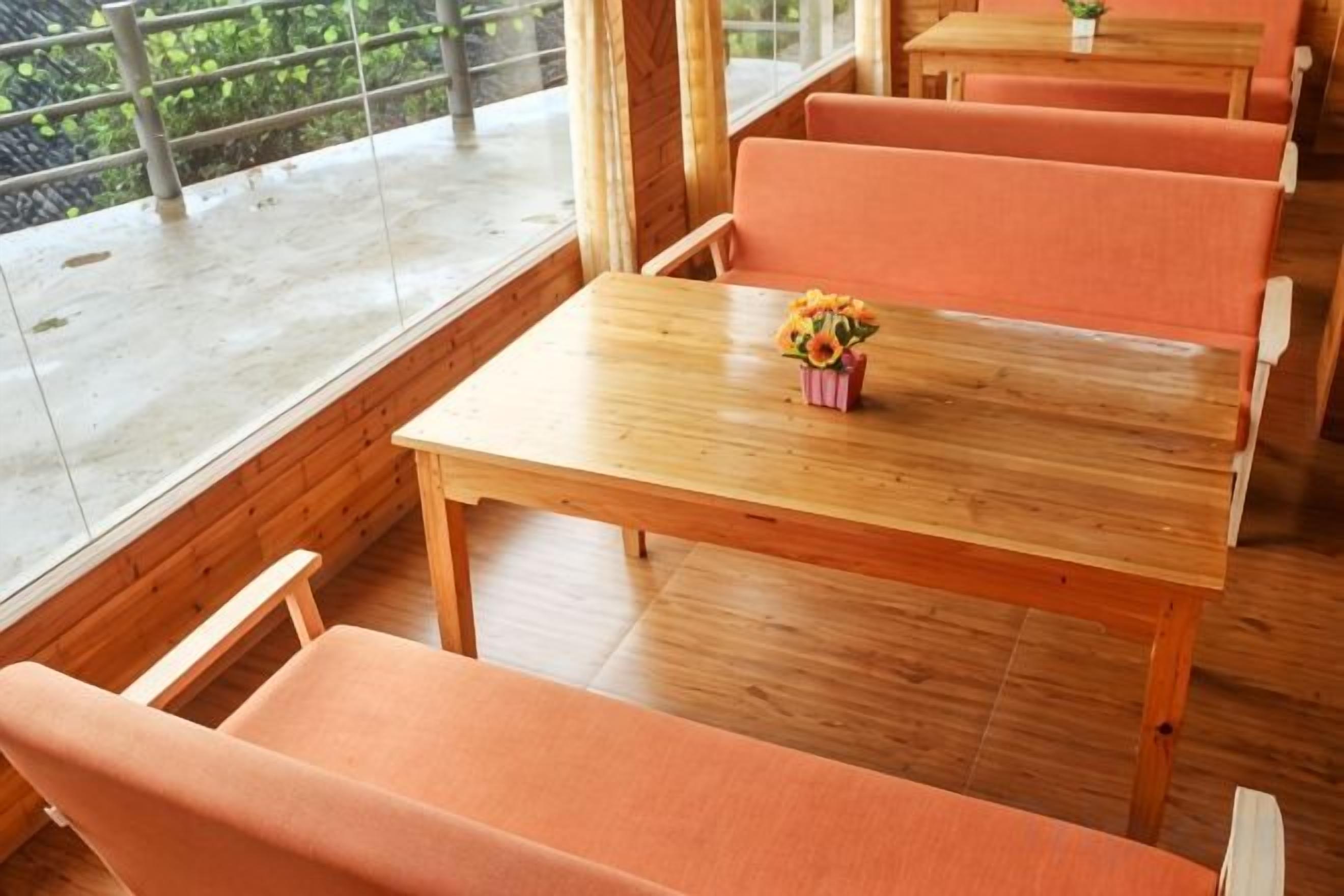 Ein Holztisch mit orangefarbenen Sitzkissen und einer Blumenvase.