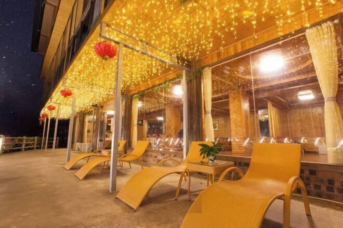 An outdoor seating area with wicker chairs and tables, under a canopy of string lights and red lanterns.