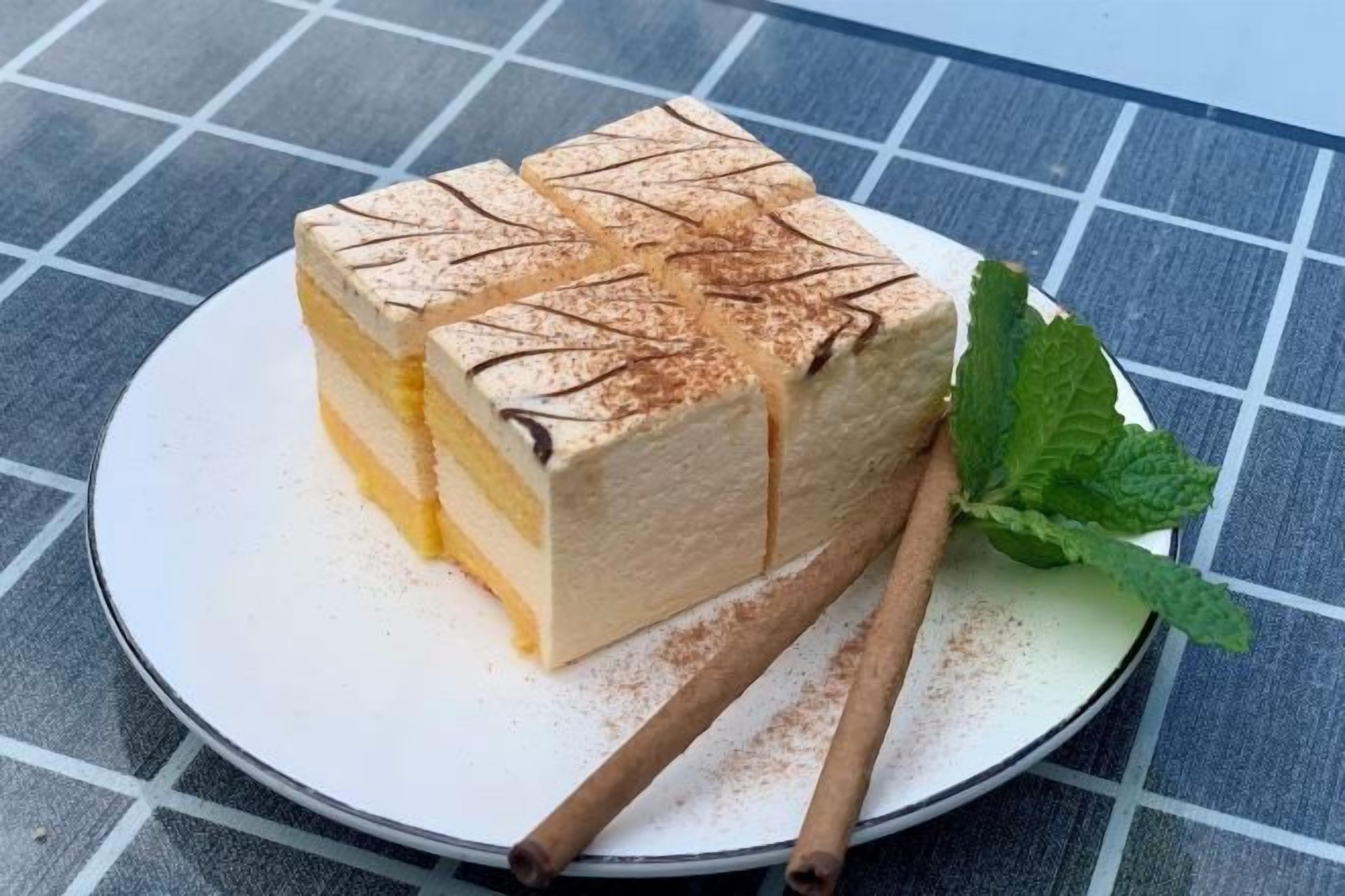 A slice of layered cake on a plate with a mint leaf and cinnamon sticks.