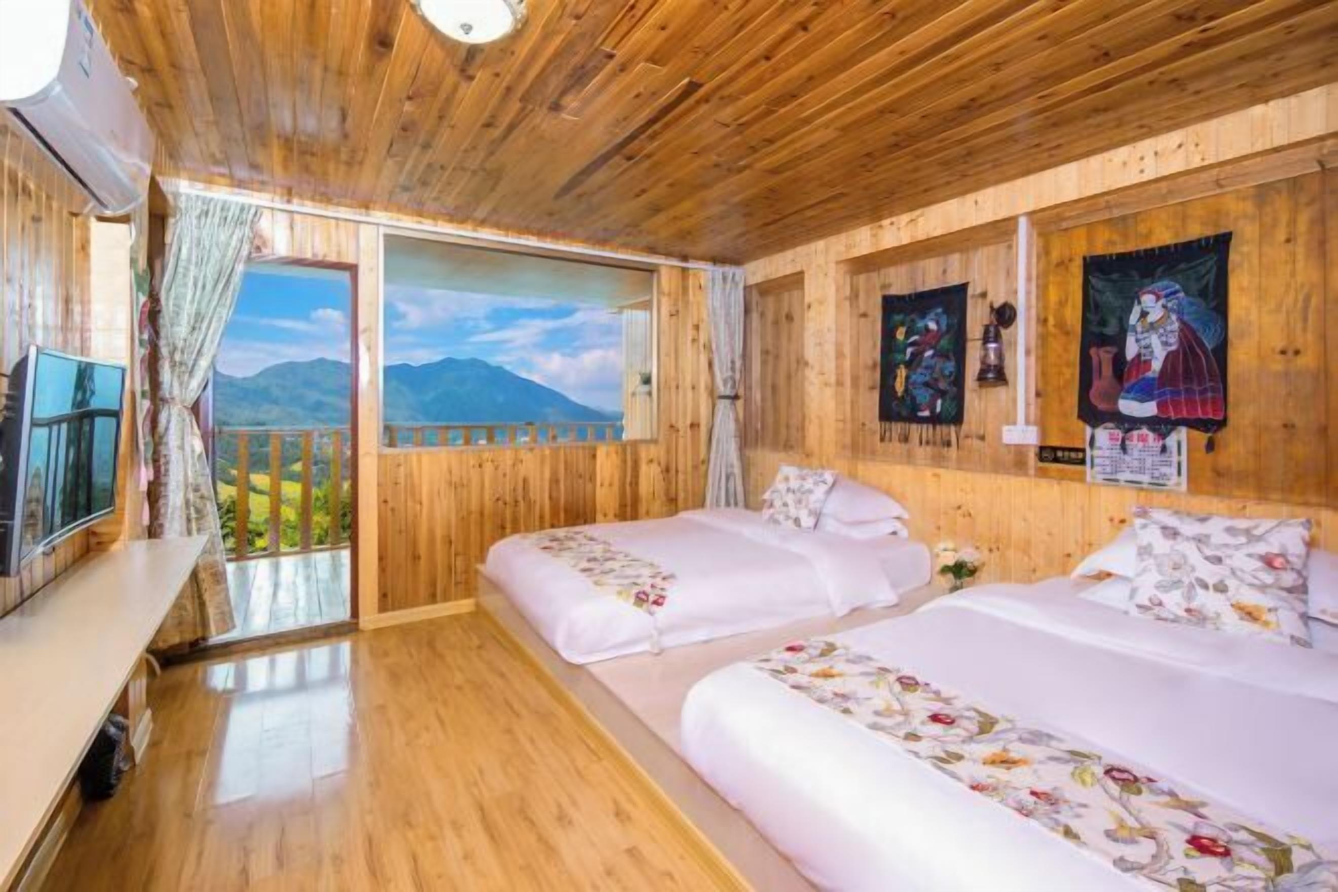 A wooden cabin room with two beds, a TV, and a scenic mountain view.
