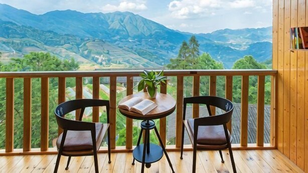 A wooden balcony with two chairs and a table, overlooking a mountainous landscape. - Xiyu Boutique Hostel (Longsheng)