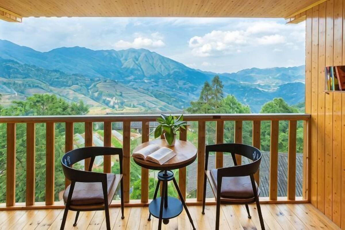A wooden balcony with two chairs and a table, overlooking a mountainous landscape.