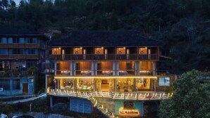 A multi-story hotel with a balcony on the second floor, a covered walkway, and several cars parked in front. - Xiyu Boutique Hostel (Longsheng)