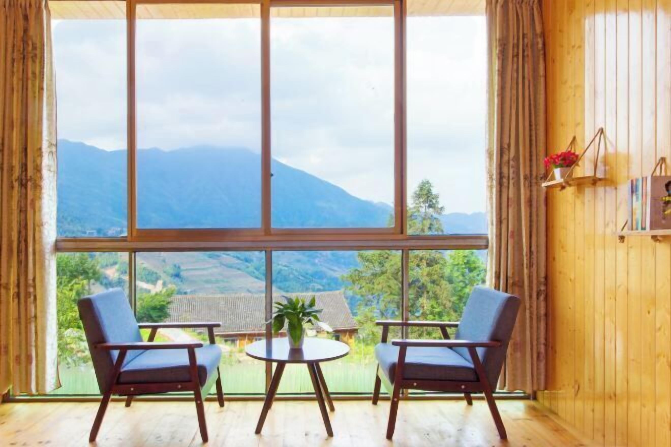 A room with large windows, two chairs, a small table, and a potted plant.