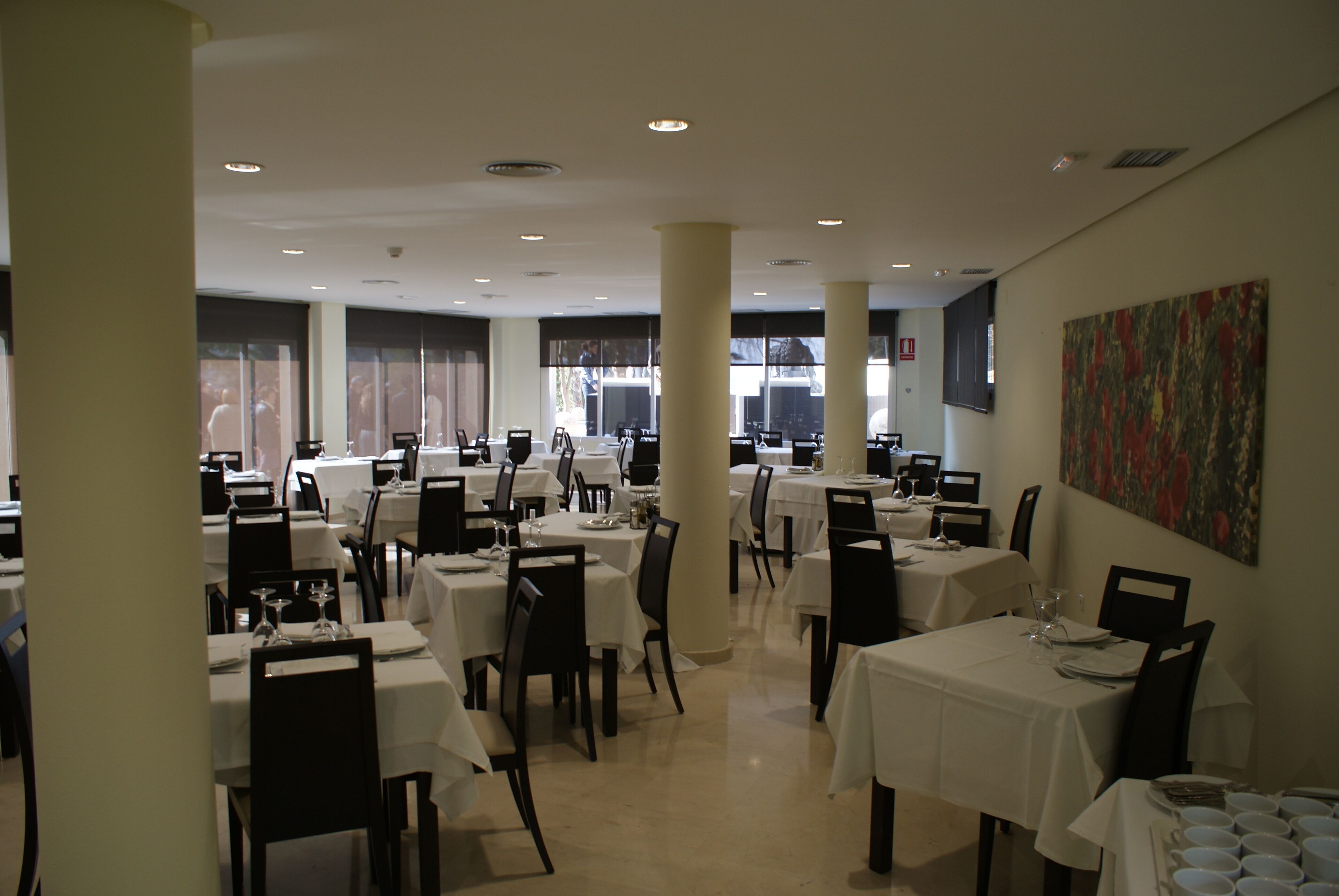 A spacious dining area with multiple tables and chairs, large windows, and a modern ceiling design.