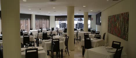 A spacious dining area with multiple tables and chairs, large windows, and a modern ceiling design.