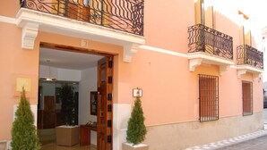 A hotel entrance with a wooden door, two potted Christmas trees, and a balcony with ornate metal railings. - UTE Hotel Villa de Biar (Biar)