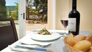 A table with a plate of food, a bottle of wine, a glass of wine, and a basket of bread. - UTE Hotel Villa de Biar (Biar)
