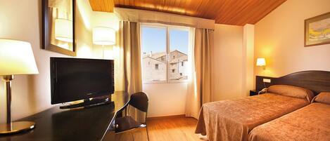 A hotel room with a bed, a desk with a TV, a chair, and a window with curtains.