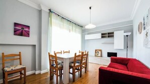 A dining area with a white table and wooden chairs, a red sofa, and a window with sheer curtains. - CAROLINA 7 - Lido di Jesolo, Italy. Entire accommodation (Lido di Jesolo)