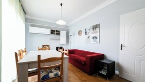 A compact living space with a dining table and chairs, a red sofa, a small black side table, and a white door. - CAROLINA 7 - Lido di Jesolo, Italy. Entire accommodation (Lido di Jesolo)