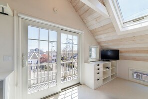 A room with a large sliding glass door, a television on a white stand, and a sloped ceiling with wooden beams.