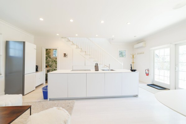 A modern kitchen with a central island, white cabinetry, and a staircase leading to an upper level.