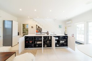 A modern kitchen with a central island, built-in shelves, and a staircase leading to an upper level. - Central, modern cottage with parking and water view (Provincetown)