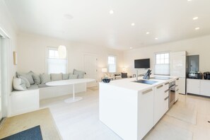 A modern kitchen with a central island, white cabinetry, and a dining area with a sofa. - Central, modern cottage with parking and water view (Provincetown)