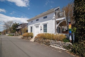 A white two-story house with a porch, a stone wall, and a rainbow flag.