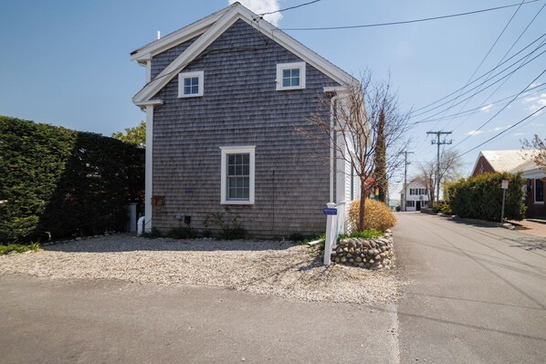 A two-story house with a gabled roof, a front porch, and a gravel driveway. - Central, modern cottage with parking and water view (Provincetown)