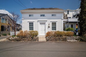 A two-story white house with a front door, a small porch, and a stone wall in front.
